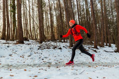 冬天穿越森林的女人寒冷冬日林间笑容满面、头戴水份的女跑步者侧视图.