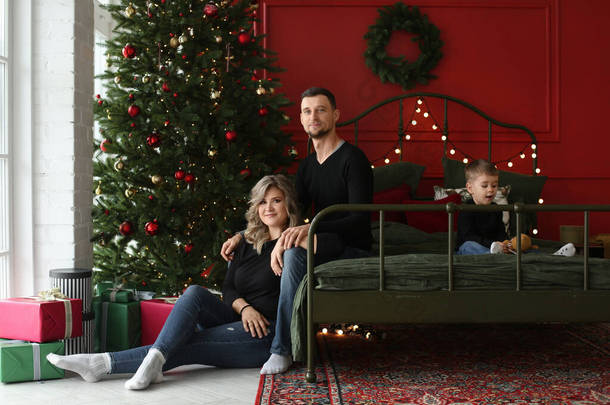 一对年轻貌美的传统夫妇，带着小可爱的儿子，在圣诞树旁摆姿势，为新年装饰。传统的家庭一起过圣诞