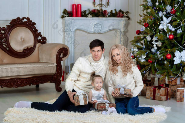 有孩子的快乐的年轻家庭坐在圣诞树旁，<strong>手里</strong>拿着礼物。礼物上有俄语新年快乐的题词。肖像。Copyspase.