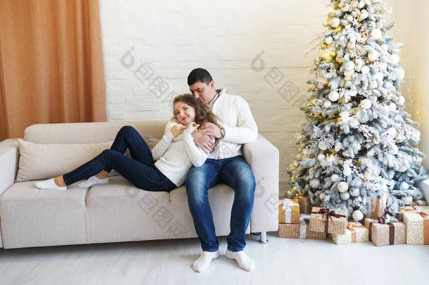 在客厅里，穿着洁白舒适的温暖毛衣，头戴圣诞树，头戴礼品盒的年轻漂亮的情侣们，面带微笑，彼此玩乐