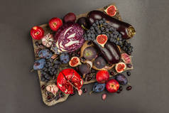 蓝色、红色和紫色食物。水果和蔬菜的烹饪背景。新鲜的无花果,李子,洋葱,茄子,葡萄,卷心菜,苹果,大蒜,山核桃,石榴.黑色石头背景，平铺