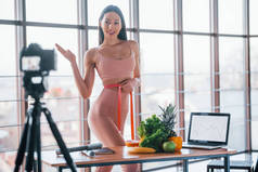 年轻的健身爱好者站在桌旁，带着健康食品和笔记本电脑，在室内做视频.