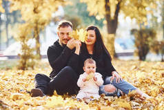 快乐的一家人坐在地上，和他们的孩子一起在美丽的秋天公园里玩乐.