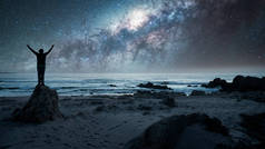 人站在岩石上，后视镜，高举双手凝视着银河，星空掠过海洋