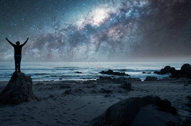 人站在岩石上，后视镜，高举双手凝视着银河，星空掠过海洋