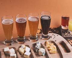 不同种类的冰啤酒放在橙色背景的乡村木桌上。啤酒，小麦，深色淡啤酒，工艺啤酒的概念。酒精饮料横幅。不同类型奶酪的奶酪盘.