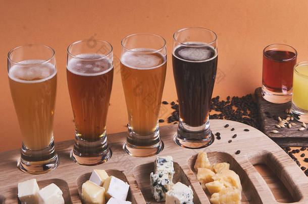 不同种类的冰啤酒放在<strong>橙色</strong>背景的乡村木桌上。啤酒，小麦，深色<strong>淡</strong>啤酒，工艺啤酒的概念。酒精饮料横幅。不同类型奶酪的奶酪盘.