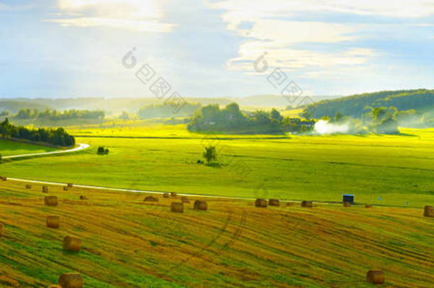 夏季全景自然景观.广阔的农村全景，有蜿蜒的道路，绿色的草地，山丘上有美丽的灯光。草包的前景.