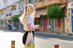 年轻的金发姑娘沿着夏季旅游城市的街道走着
