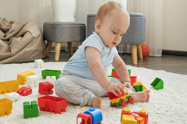 可爱的小男孩坐在地毯上，玩着五颜六色的塑料<strong>玩具车</strong>。家庭中<strong>儿童</strong>发展、教育和创造力的概念