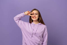 一个漂亮的、乐观的少女的画像，近视，站在紫色的背景上。穿着紫色连帽衫的年轻情绪化女人