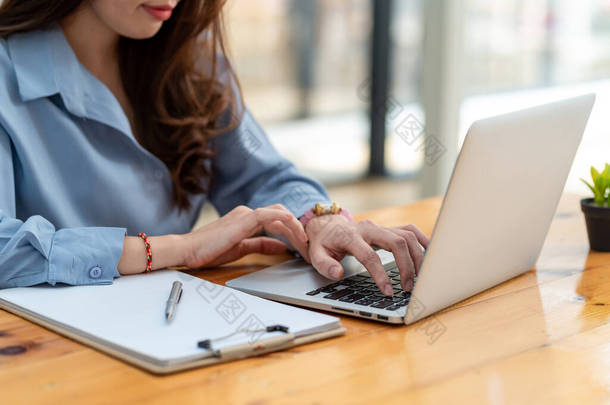 Close-up of a business woman's hand typing using a laptop in the <strong>office</strong>.