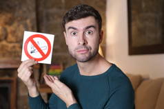 close-up portrait of handsome young man holding no smoking sign at home