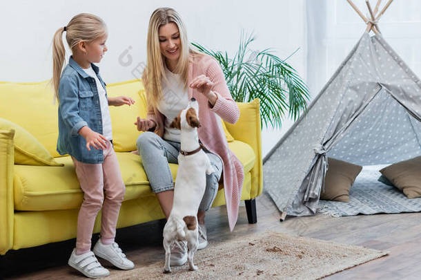 Smiling woman feeding jack russell terrier near kid at home, <strong>banner</strong> 