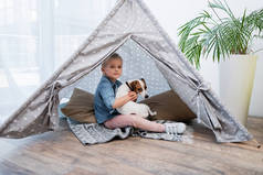 Kid hugging jack russell terrier in tepee at home 