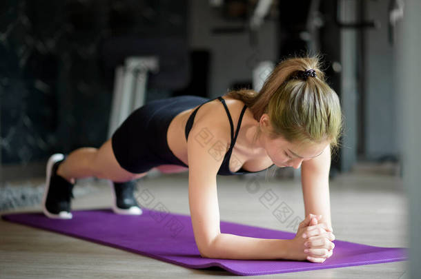 一个快乐而美丽的女人正在体育馆的垫子上做瑜伽板，树立健康生活方式、运动、训练、健康和运动的观念. 