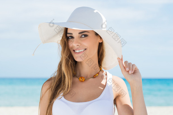 在白色太阳帽<strong>放松</strong>在海滩上的年轻女子