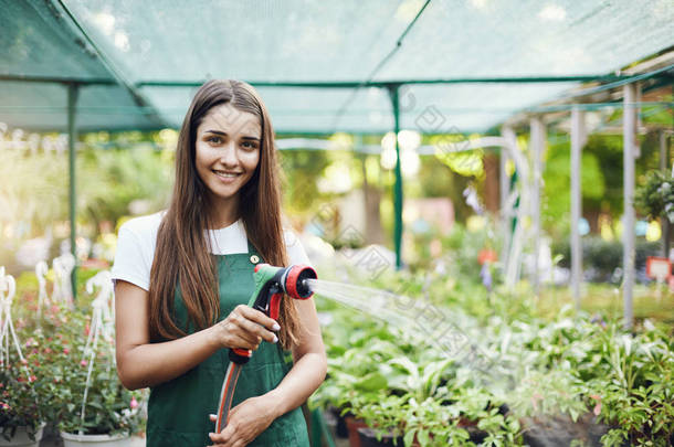 快乐的<strong>年轻女</strong>园丁浇灌植物所有者经营的温室存储区中.