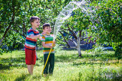 可爱的小男孩浇水植物与浇水软管在花园里