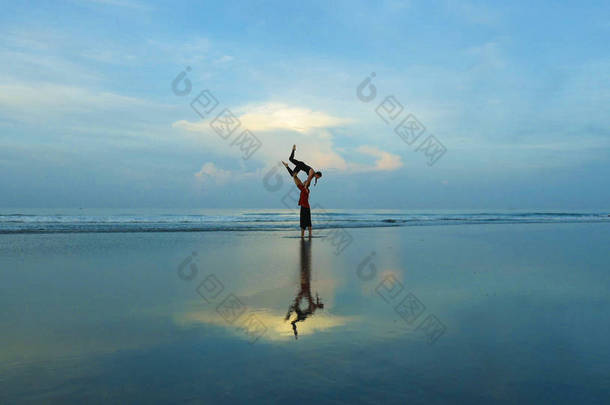 健康和有吸引力的适合夫妇的杂技演员做杂技平衡和冥想练习在美丽的沙漠海滩练习平衡和和谐姿势