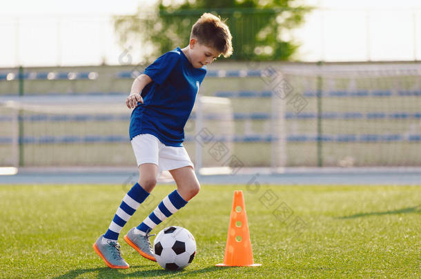 穿着足球制服的男孩用球练习。孩子们在草地体育场踢球.年轻运动员在训练场提高了足球运球技术.少年足球运动员流着口水穿过圆锥