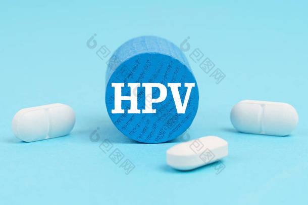 医学和健康概念。药丸躺在蓝色的表面，一个木制的蓝色圆筒，上面刻着：HPV