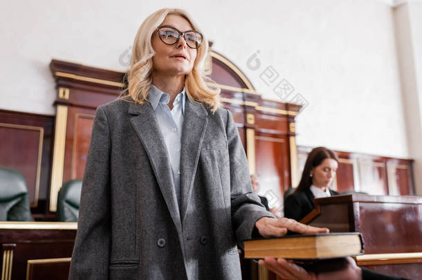 戴眼镜的女人在法庭上对《圣经》宣誓，接近检察官，背景模糊