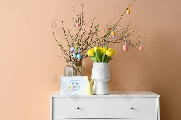 用彩绘的鸡蛋、郁金香和贺卡装饰的树枝，在彩色墙壁附近的抽屉盒上印有<strong>HAPPY</strong> EASTER字样