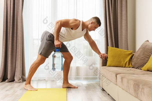 年轻的运动员用一大瓶水代替哑铃进行家庭锻炼