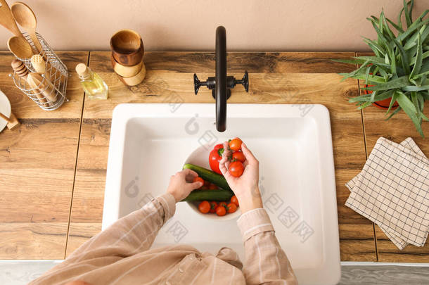 在米色墙壁附近的水槽里洗新鲜蔬菜的女人