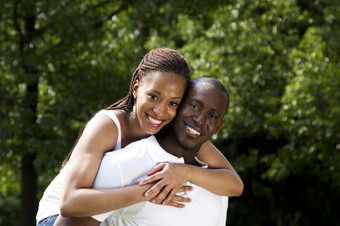 美丽的快乐微笑年轻的非洲美国夫妇爱穿白色衬衫女人拥抱男人。与树的背景
