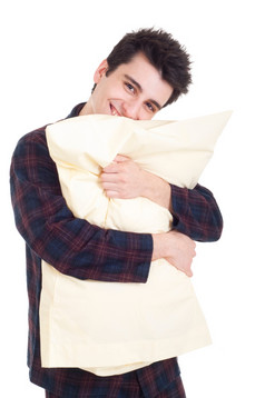 微笑年轻的男人。睡衣持有枕头孤立的白色背景