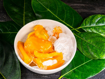 甜点菠萝蜜糖浆与椰子牛奶和冰白色碗绿色菠萝蜜叶和木背景