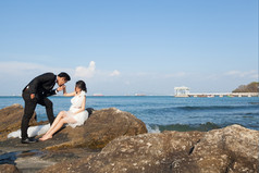 新娘而且新郎新娘婚礼衣服坐着的岩石的海