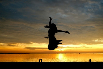 轮廓女人跳的海与美丽的日落背景