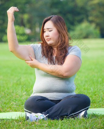 年轻的亚洲脂肪女人检查她的手臂脂肪
