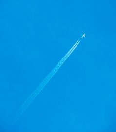 飞机飞行通过清晰的蓝色的天空与蒸汽小径