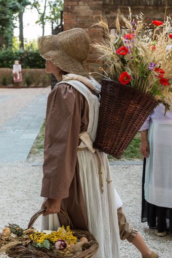 柳条篮子填满与捆小麦和红色的花进行在的肩膀年轻的村姑