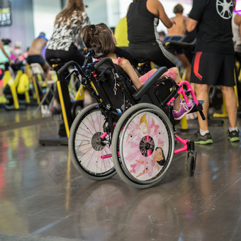 女孩粉红色的轮椅参加健身锻炼与旋转自行车女孩粉红色的轮椅参加健身锻炼与旋转自行车