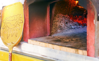 木烤箱为烘焙披萨与灰烬燃烧余烬和火倾斜对的烤箱在那里黄色的铲取的披萨从的烤箱一次准备好了