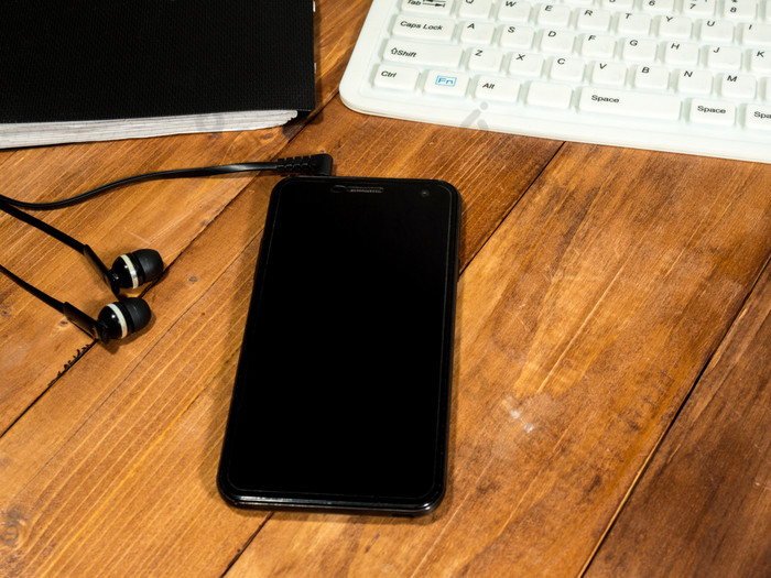 工作空间木表格与白色键盘黑色的智能手机与耳机和日记