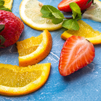 分类不同的水果和浆果草莓片橙色柠檬和薄荷叶子平躺前视图蓝色的背景草莓片橙色柠檬和薄荷叶子平躺前视图