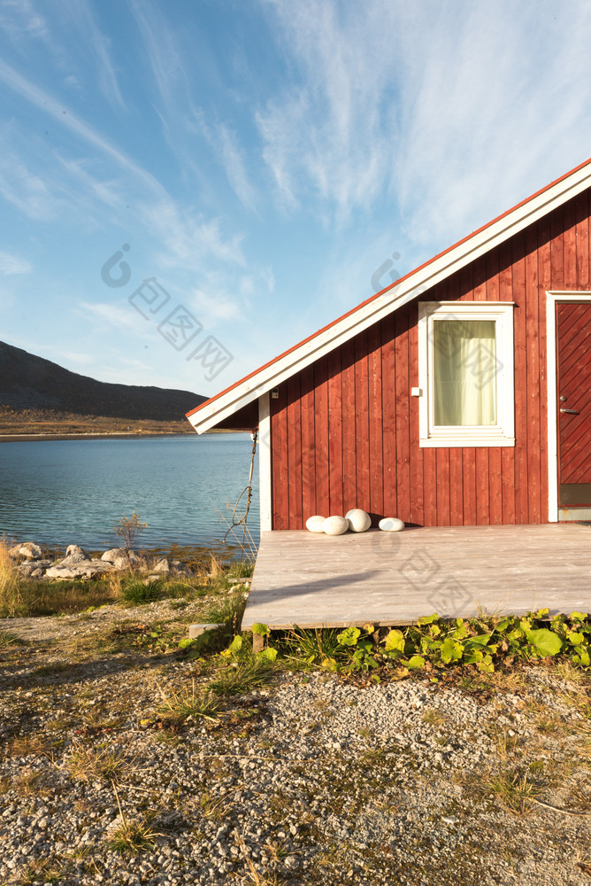 视图木挪威海滩小屋与石头的海岸线俯瞰的特罗姆瑟峡湾北极圆挪威和山峰阳光明媚的蓝色的天空一天
