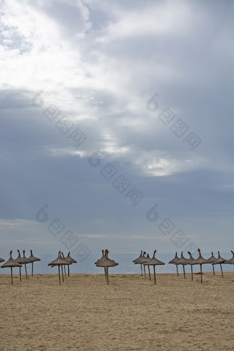 美丽的沙子海滩和稻草阳<strong>伞下</strong>多云的天空11月马略卡岛西班牙美丽的沙子海滩和稻草阳<strong>伞下</strong>多云的天空