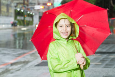年轻的女孩雨穿绿色雨衣而且持有红色的伞人行道上下一个街