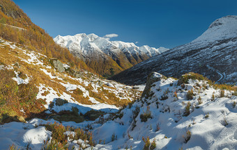 挪威山景观雪覆盖山坡上与长满青苔的岩石遥远的白雪覆盖的山和太阳闪亮的