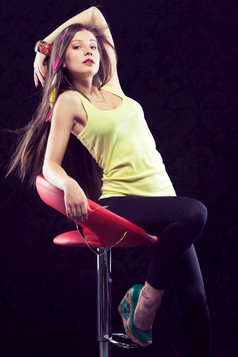 年轻的美丽的女人与色彩斑斓的羽毛长头发坐着红色的椅子黑色的背景健美的图像