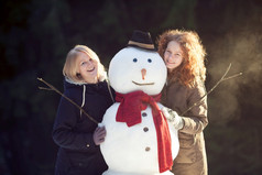 两个微笑漂亮的女孩摆姿势与雪人森林焦点雪人