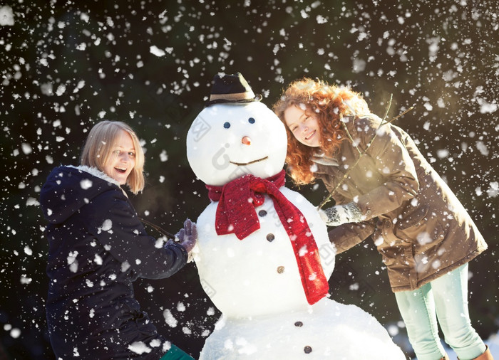 两个快乐漂亮的女孩享受建筑雪人雪冬天一天