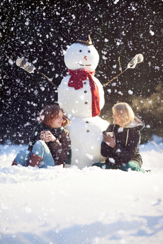 两个年轻的女人坐着附近雪人和喝热茶而rsquo下雪